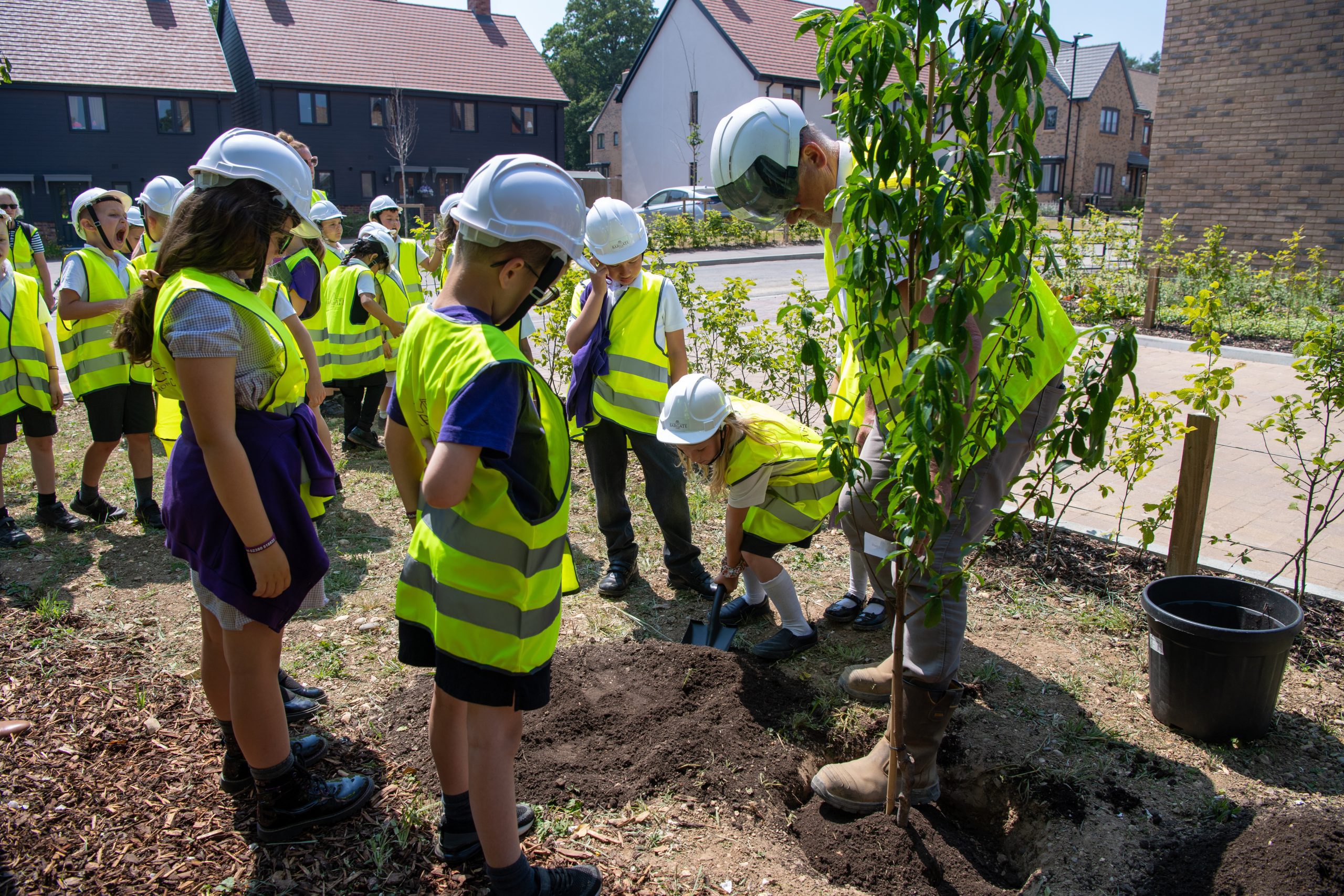 School children visiting Bargate Homes development wearing safety vests and planting a tree