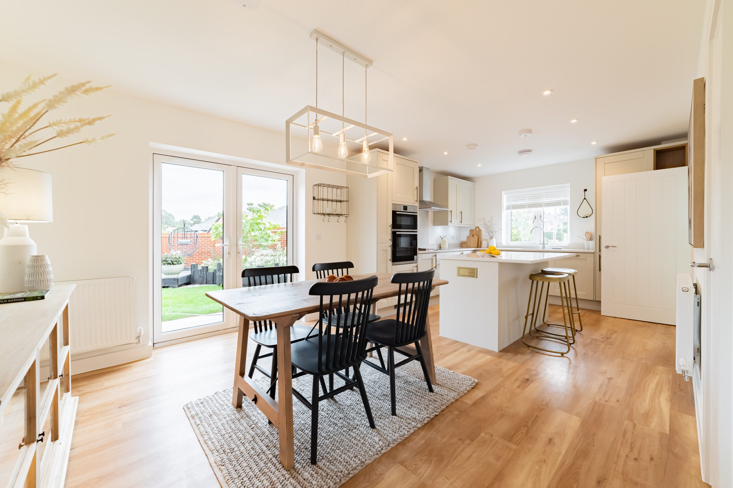 Bright open-plan kitchen and dining area with wooden floors, black chairs, and island counter